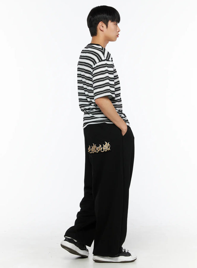 Men's Flame Wide Sweatpants (Black) IL514 side view on male model standing with hands in pockets, styled with black and white striped henley tee and sneakers