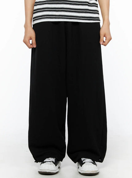 Men's Flame Wide Sweatpants (Black) IL514 front close-up on model showing wide-leg silhouette, elastic waist, and balloon fit with drawstring hem and sneakers