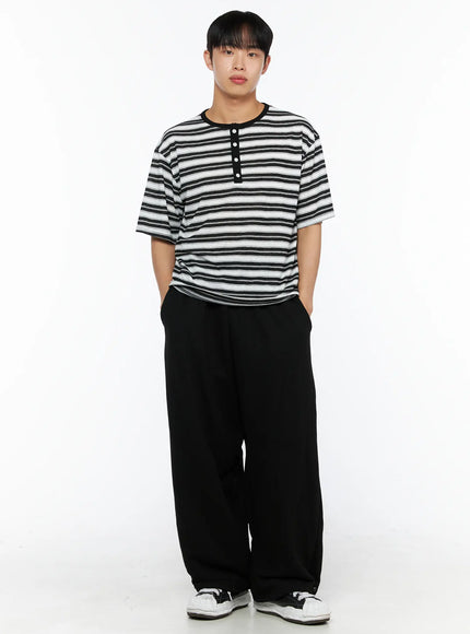 Men's Flame Wide Sweatpants (Black) IL514 front full view on male model standing with hands in pockets, showing wide-leg fit and striped henley tee styling