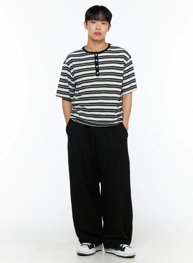 Men's Flame Wide Sweatpants (Black) IL514 front full view on male model standing with hands in pockets, showing wide-leg fit and striped henley tee styling