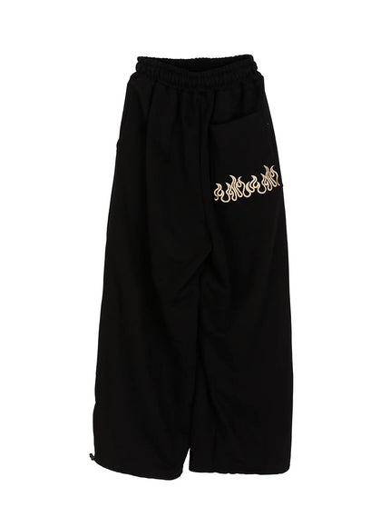 Men's Flame Wide Sweatpants (Black) IL514 flat-lay front view with gold and white flame embroidery on right thigh pocket, elastic waist, and hem drawstring toggles