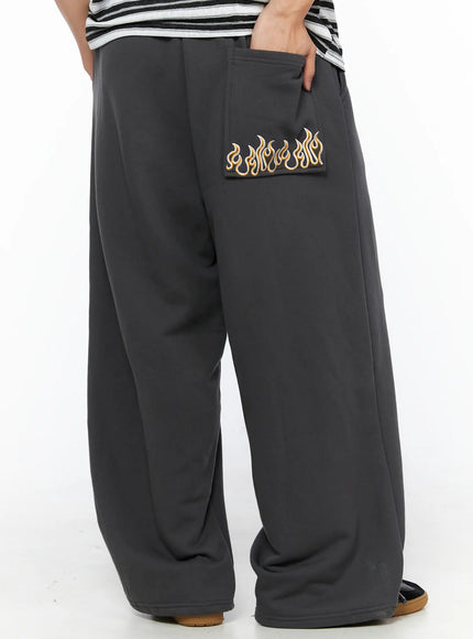 LEWKIN Men's Flame Wide Sweatpants (Dark Gray) IL514 Dark gray angled back close-up on model showing gold flame embroidery on back pocket, wide-leg fleece