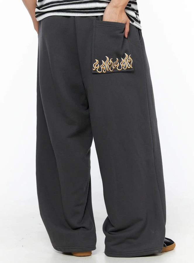 LEWKIN Men's Flame Wide Sweatpants (Dark Gray) IL514 Dark gray angled back close-up on model showing gold flame embroidery on back pocket, wide-leg fleece