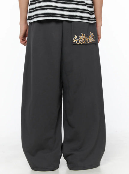 Men's Flame Wide Sweatpants (Dark Gray) IL514 Dark gray back three-quarter view on male model showing gold flame embroidery on back pocket and wide-leg drop