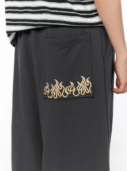 Men's Flame Wide Sweatpants (Dark Gray) IL514 Dark gray close-up detail of back pocket with gold and white flame embroidery on fleece fabric