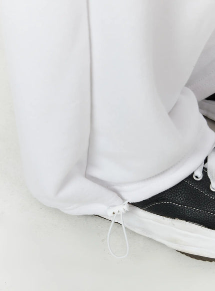 Men's Flame Wide Sweatpants (White) IL514 White close-up detail of hem and drawstring ankle tie on wide-leg fleece trouser leg, resting over black leather sneaker