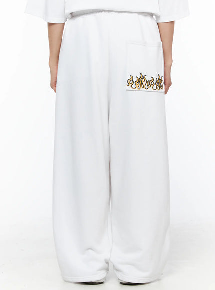 LEWKIN Men's Flame Wide Sweatpants (White) IL514 White M/L back view on female model showing gold and black flame embroidery on rear pocket, wide-leg fleece fit