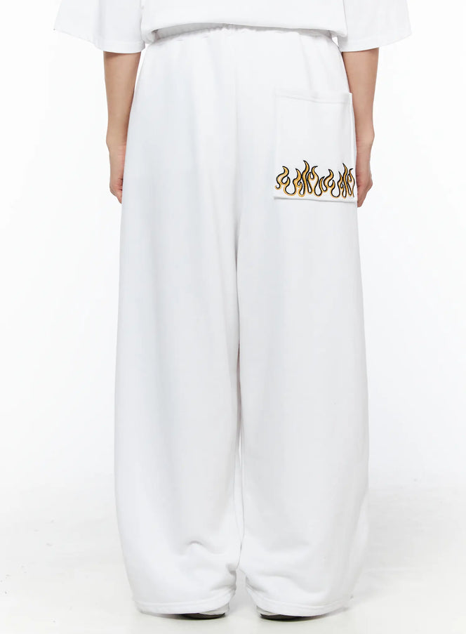 LEWKIN Men's Flame Wide Sweatpants (White) IL514 White M/L back view on female model showing gold and black flame embroidery on rear pocket, wide-leg fleece fit