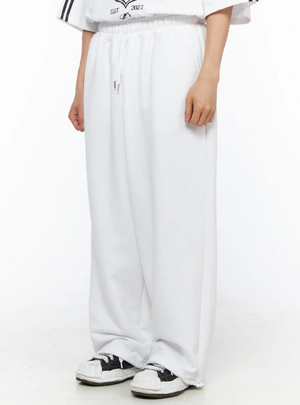 Men's Flame Wide Sweatpants (White) IL514 White angled front close-up on male model showing drawstring waistband, wide-leg silhouette and side seam, paired with sneakers