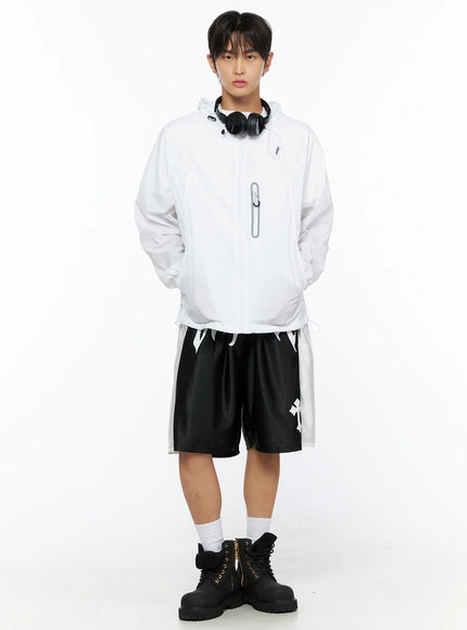 Men's Gothic Print Athletic Shorts IL515 Black full-body front styling shot on male model with white windbreaker and headphones, cross print on shorts leg