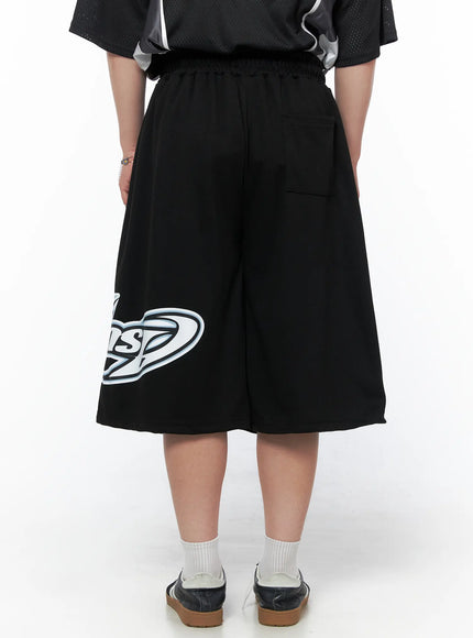 Men's Graphic Logo Shorts (Black) IL502 black back view on model cropped waist-down revealing back pocket elastic waistband and partial logo print on left leg