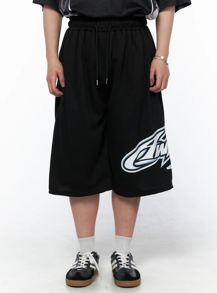 LEWKIN Men's Graphic Logo Shorts (Black) IL502 black front view on model cropped waist-down standing straight with drawstring waist and oversized logo print