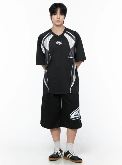 Men's Graphic Logo Shorts (Black) IL502 black full-length front view on male model standing straight paired with black mesh jersey and sneakers showing bold logo print