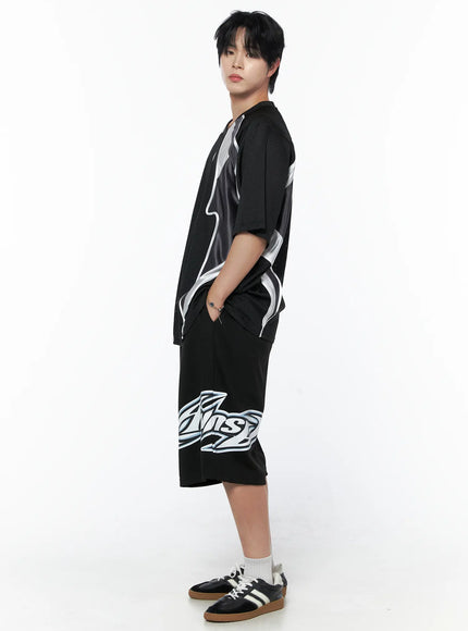 Men's Graphic Logo Shorts (Black) IL502 black side view on male model full-length styled with matching mesh jersey and sneakers showing logo graphic at hem