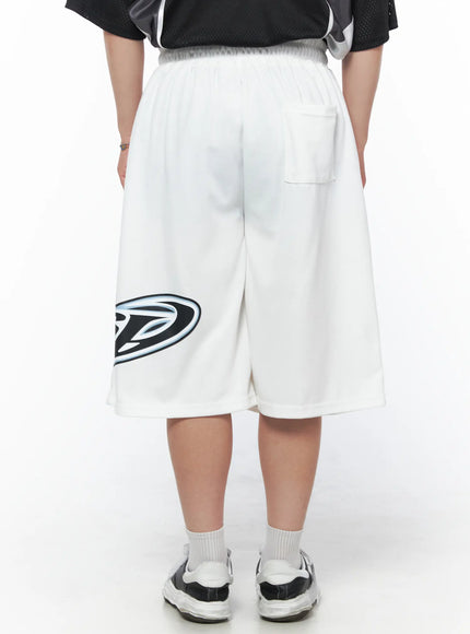 Men's Graphic Logo Shorts (White) IL502 White three-quarter back view on male model styled with black mesh jersey, logo print visible on front leg, sneakers