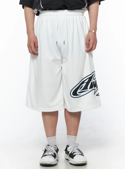 Men's Graphic Logo Shorts (White) IL502 White front view on model standing, drawstring elastic waist, oversized fit with bold logo graphic on right leg