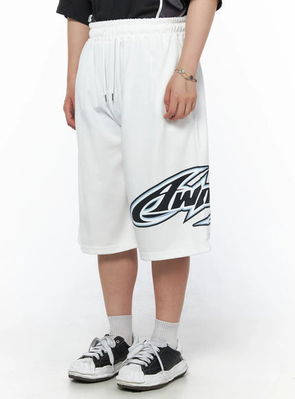 Men's Graphic Logo Shorts (White) IL502 White side view on model standing still, full graphic logo visible across lower leg, relaxed wide fit, white sneakers