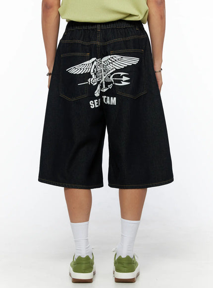 Men's Graphic Loose-Fit Shorts IL515 Dark blue back view on female model showing SEAL TEAM eagle graphic print, wide-leg denim with elastic waist and contrast stitching