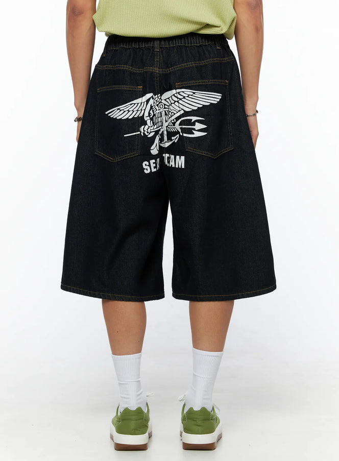 Men's Graphic Loose-Fit Shorts IL515 Dark blue back view on female model showing SEAL TEAM eagle graphic print, wide-leg denim with elastic waist and contrast stitching