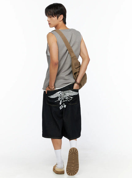 Men's Graphic Loose-Fit Shorts IL515 Dark blue back diagonal view on male model with crossbody bag and waffle tank top, SEAL TEAM graphic print visible on wide-leg denim