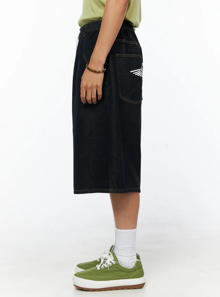 Men's Graphic Loose-Fit Shorts IL515 Dark blue side view on female model showing back pocket with wing graphic detail, wide-leg denim silhouette and green sneakers