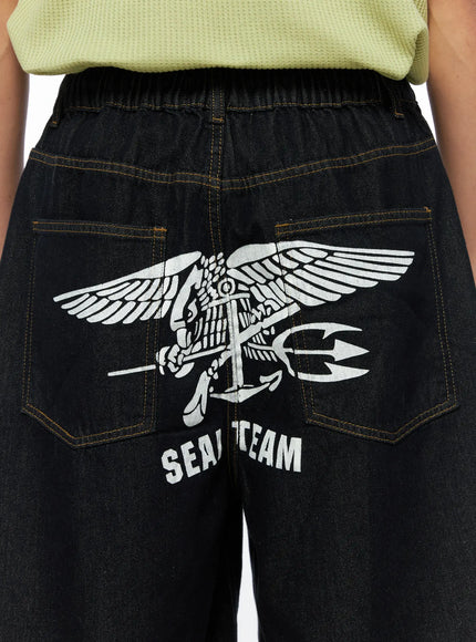 Men's Graphic Loose-Fit Shorts IL515 Dark blue close-up back detail on female model showing SEAL TEAM eagle anchor graphic print across back panel with contrast stitching