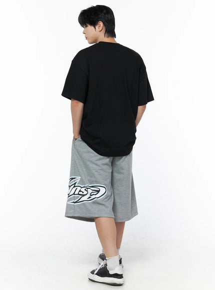 Men's Graphic Oversized T-Shirt IL502 Black back shot on male model full body, plain back with dropped shoulders, paired with gray graphic shorts and sneakers, side-facing pose