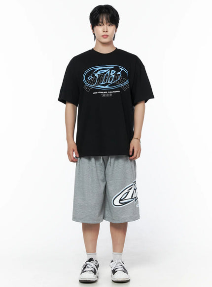 Men's Graphic Oversized T-Shirt IL502 Black front shot on male model full body standing, blue oval logo graphic, crew neck, relaxed fit, paired with gray shorts and sneakers