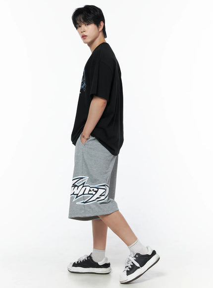 Men's Graphic Oversized T-Shirt IL502 Black side shot on male model walking pose, blue chest graphic visible, oversized silhouette, paired with gray printed shorts and sneakers