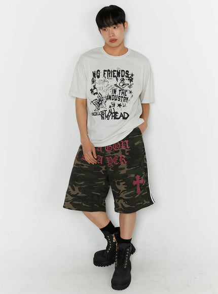 Men's Graphic Pigment Dyed Tee IL514 Light beige full-body front shot on male model standing with hands in pockets styled with camo shorts and boots