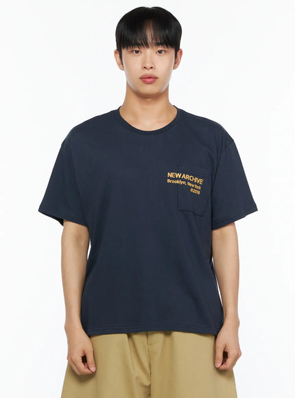 Men's Graphic Pocket Tee IL514 Navy close-up front view on male model showing yellow NEW ARCHIVE Brooklyn New York ©2018 chest pocket graphic and boxy cotton fabric texture
