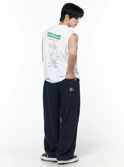 Men's Graphic Print Sleeveless Tee IL502 White three-quarter back shot on male model showing back graphic print and wide armhole cut with navy pants
