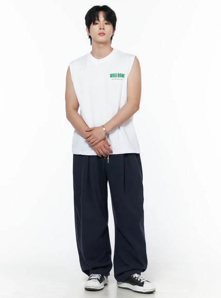 Men's Graphic Print Sleeveless Tee IL502 White front shot on male model hands clasped at waist full-length view with navy wide-leg pants and sneakers
