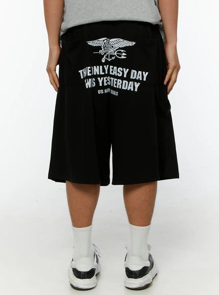 LEWKIN Men's Graphic Print Sweat Shorts IL515 Black back view on model wearing gray graphic tee and sneakers, US Navy Seals eagle and text print
