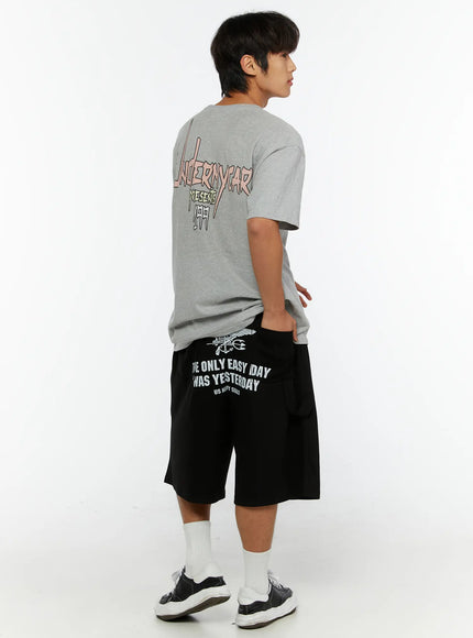 Men's Graphic Print Sweat Shorts IL515 Black side-angle full-body view on male model with gray tee, back graphic print visible, sneakers