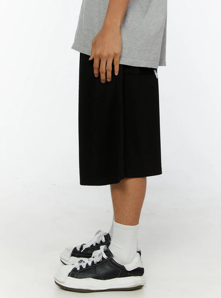 Men's Graphic Print Sweat Shorts IL515 Black side view on male model showing back graphic print, wide boxy leg hem, styled with gray tee