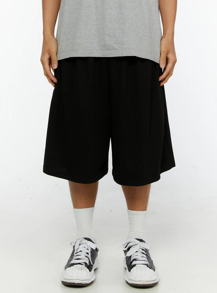 Men's Graphic Print Sweat Shorts IL515 Black front close-up on model showing elastic waistband, wide-leg silhouette, cotton fabric texture