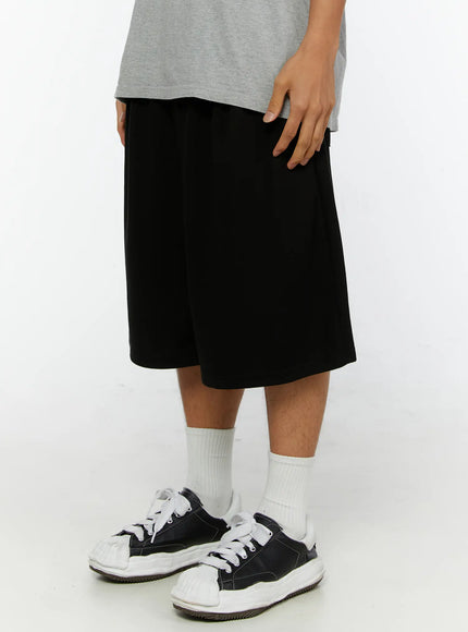 Men's Graphic Print Sweat Shorts IL515 Black side close-up on model showing relaxed wide-leg cut, side pocket detail and woven label tag