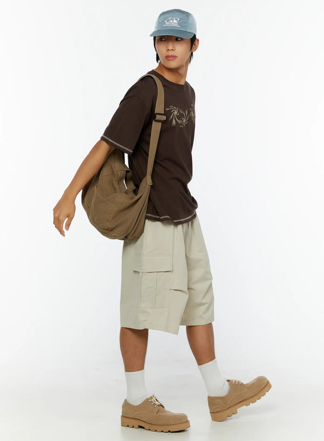Men's Graphic Print T-Shirt IL513 Dark brown full-body side view on male model walking with olive canvas crossbody bag blue cap and cargo shorts