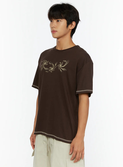 Men's Graphic Print T-Shirt IL513 Dark brown side view on male model turned slightly left showing swirl graphic print and contrast stitch hem detail
