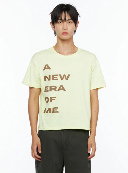 Men's Graphic Semi-Crop T-Shirt IL528 light yellow close-up front shot on male model waist-up highlighting oversized brown A NEW ERA OF ME stacked letter print