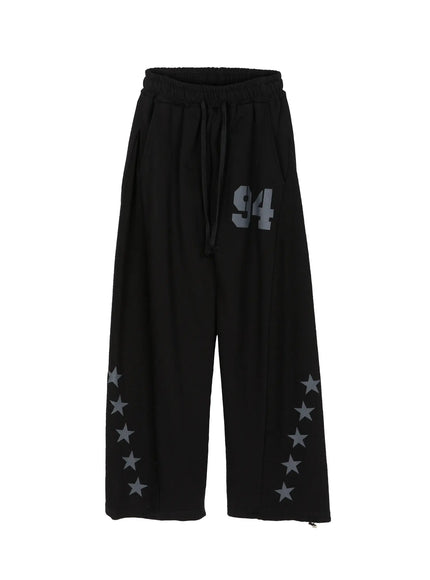 Men's Graphic Sweatpants (Black) IU529 Black flat-lay front view, wide-leg sweatpants with drawstring waist, '94' graphic on thigh, and charcoal star prints along hem