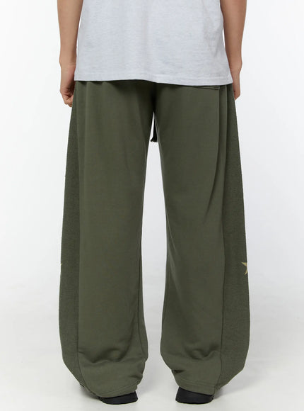 Men's Graphic Sweatpants (Dark Green) IU529 Dark green back view on model showing smooth center panel, textured fleece side panels, tassel drawstring, and gold star hem detail