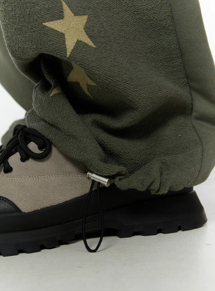 Men's Graphic Sweatpants (Dark Green) IU529 Dark green close-up detail of hem showing gold star print on fleece panel, adjustable drawcord stopper at ankle cuff
