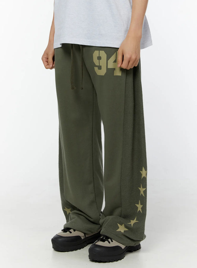 Men's Graphic Sweatpants (Dark Green) IU529 Dark green angled front view on model highlighting 94 graphic, wide ultra-baggy leg with star-print fleece side panel