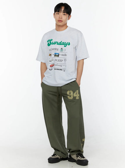 Men's Graphic Sweatpants (Dark Green) IU529 Dark green full-body front shot on male model styled with grey graphic tee, showing relaxed wide-leg fit and gold star hem print