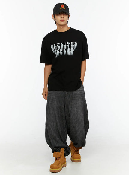 Men's Graphic T-Shirt IL515 Black full-body front view on standing male model, oversized silhouette with distressed gothic letter print, styled with baggy jeans