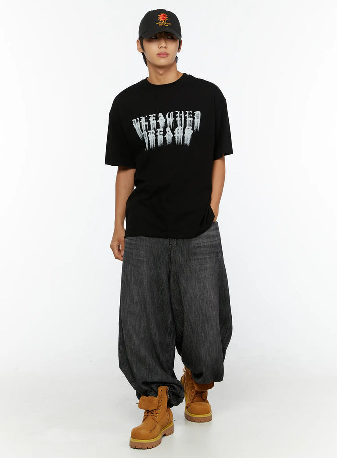 Men's Graphic T-Shirt IL515 Black full-body front view on standing male model, oversized silhouette with distressed gothic letter print, styled with baggy jeans