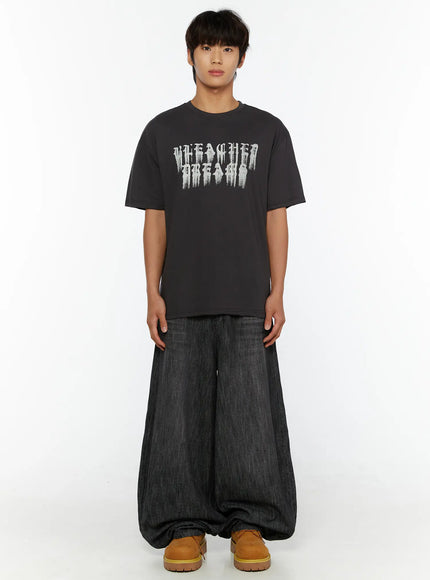 Men's Graphic T-Shirt IL515 Charcoal front view on standing male model, oversized short-sleeve tee with gothic Bleached Dreams graphic print, paired with wide-leg jeans