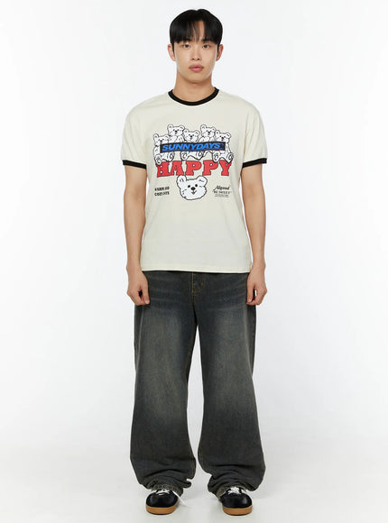 Men's Graphic T-Shirt IU529 Light beige front view on male model standing straight arms down black ringer collar and cuffs SUNNYDAYS HAPPY bear graphic styled with dark wash wide-leg jeans
